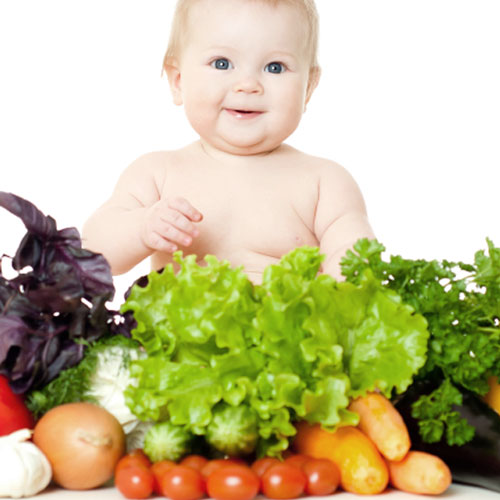 infant baby sitting with various vegetables on display in front