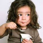 toddler girl eating yogurt with a spoon to her mouth.